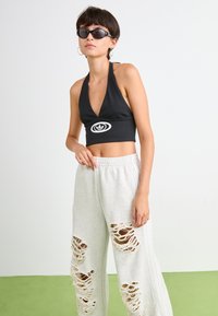Must mustatsiooniga must kaeluse crop top, koos heledate hallide dressipükstega, kus on suured kulunud lõiked. Aksessuaarideks tumedad prillid.
