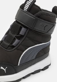 Black and gray mid-top athletic shoe with synthetic material, padded collar, Velcro strap, and rubber outsole featuring traction lugs.