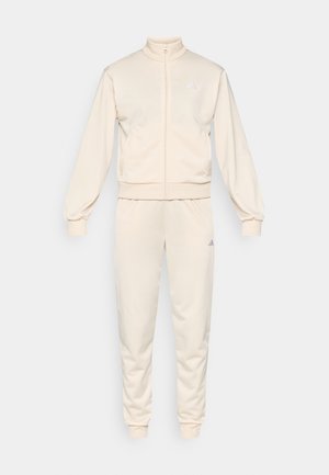 Beige tracksuit with a high collar, full zip, and ribbed cuffs. Features embroidered logo in light purple on the jacket and pants.