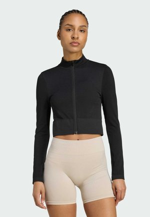 Black cropped zip-up jacket with long sleeves, made of soft fabric; paired with light beige high-waisted shorts, featuring a smooth texture.