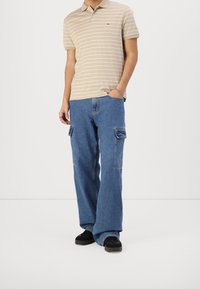 Beige gestreepte polo met een kraag, gecombineerd met losse blauwe denim cargobroeken met zijzakken en een relaxed fit. Zwarte sneakers.