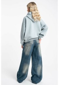 Jasnoniebieska, oversize bluza z kapturem; zestawiona z luźnymi, jasnoniebieskimi dżinsami. Dżinsy mają przetarty wygląd i tylne kieszenie.