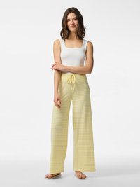 Witte tanktop met vierkante hals, gedragen met gele en witte gestreepte wijde broek, met een trekkoord in de taille en een relaxte pasvorm. Minimalistische slippers.