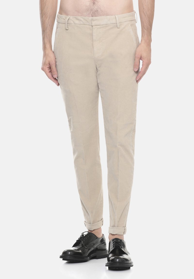 Pantaloni in cotone beige con taglio affusolato, tasche anteriori e orli arrotolati, abbinati a scarpe in pelle nera con lacci.