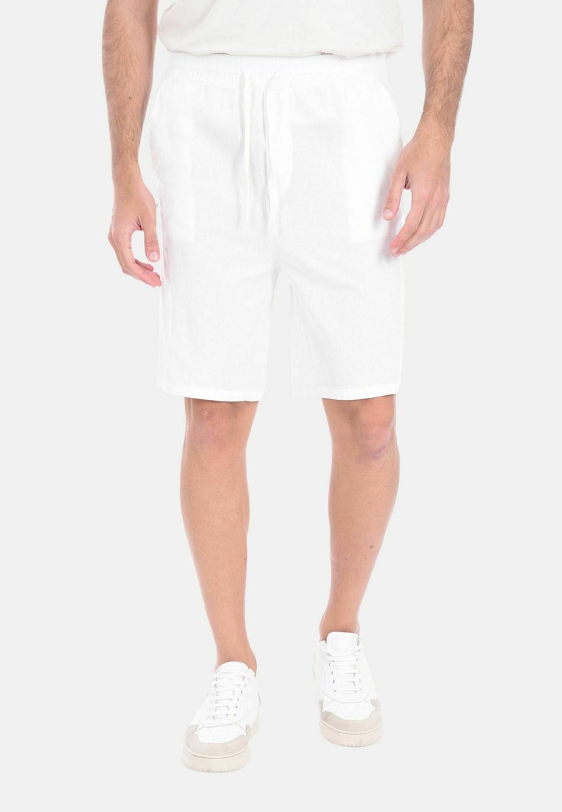 Shorts bianchi in lino con vita elasticizzata e cordoncino, dotati di tasche laterali e taglio rilassato. Indossati con sneakers bianche.