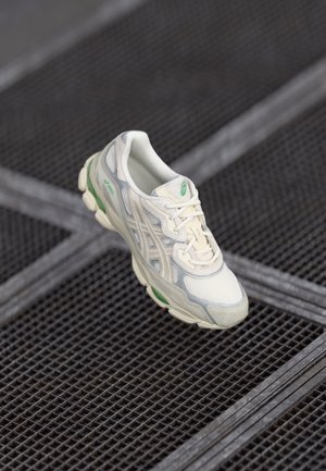 White athletic shoe with a mesh upper, green accents, and a textured sole. Features a rounded toe and lacing system for a secure fit.