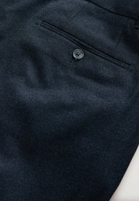 Dark blue fabric trousers featuring a textured weave, single button closure, and a standard pocket with a curved opening detail.