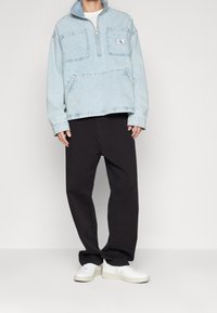 Ljusblå denimtröja med kvartsdagsdragkedja, två framfickor och ett patch-logotyp. Kombinerad med svarta lösa byxor och vita sneakers.