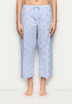 Mujer con pantalones de pijama de rayas azul claro con pequeños patrones de rosas rosas, cintura con cordón, de pie descalza frente a un fondo liso.