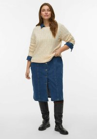 Suéter beige de punto trenzado combinado con una falda de mezclilla con botones en la parte delantera y una abertura. Botas negras altas hasta la rodilla completan el atuendo.
