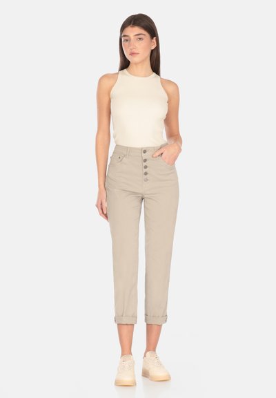 Pantaloni beige a vita alta con chiusura a bottone e risvolti, abbinati a una canotta in maglia cotone color crema e sneakers chiare.