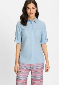 Light blue button-up shirt with rolled sleeves, two chest pockets, and a smooth texture, paired with patterned multi-colored pants.