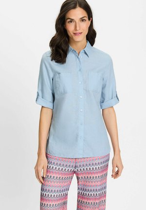 Hellblaue button-up Hemd mit hochgeschobenen Ärmeln, zwei Brusttaschen und einer glatten Textur, kombiniert mit gemusterten, mehrfarbigen Hosen.