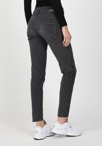 Graue, schmal geschnittene Hosen mit einer glatten Textur, mittelhohem Bund und zwei Gesäßtaschen. Kombiniert mit weißen Sneakern.