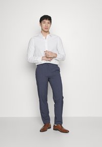 White long-sleeve button-up shirt, navy trousers, brown dress shoes. Smooth fabric with a fitted design, standing against a plain background.