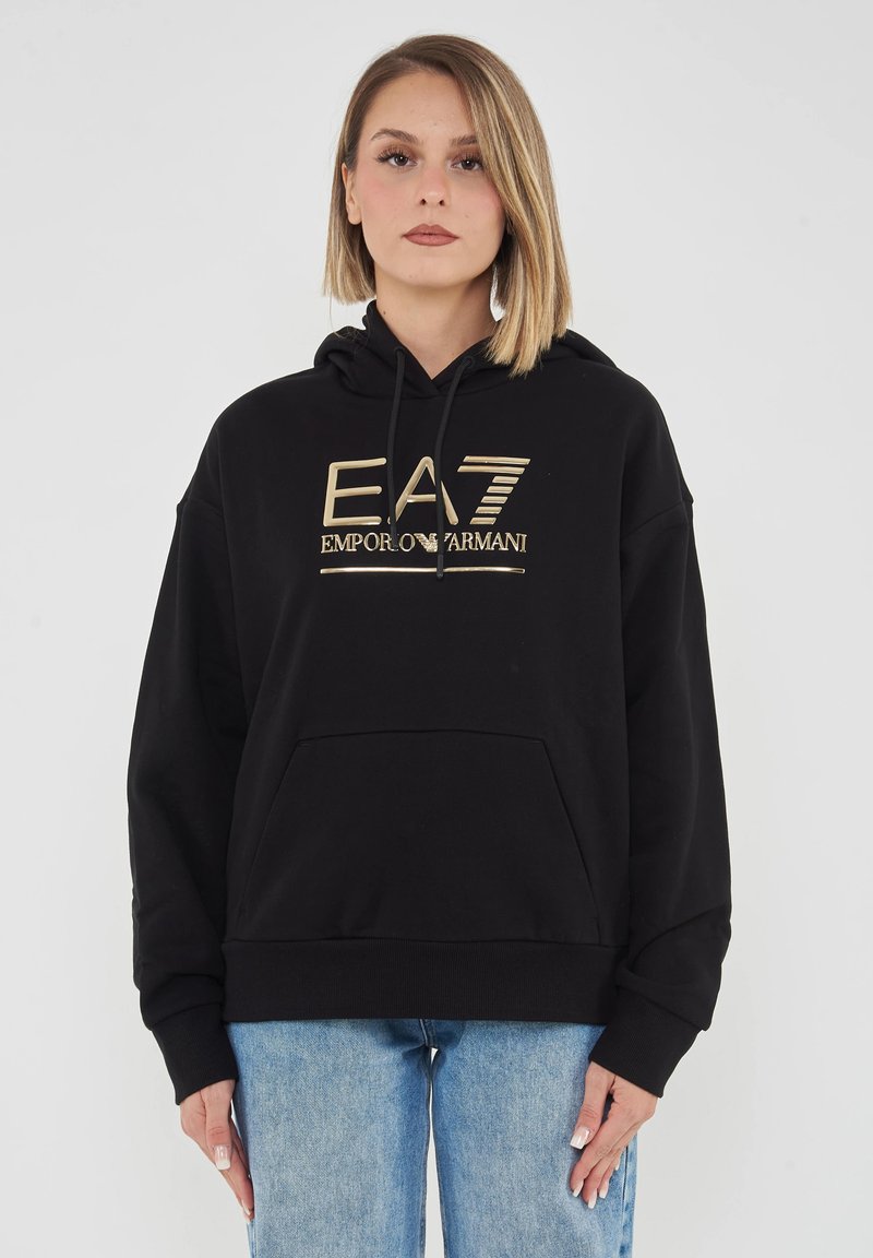 Felpa nera in misto cotone con tasca frontale, cappuccio con coulisse e logo dorato. Indossata con jeans di denim azzurri.