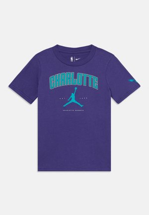 Violet cotton t-paita, jossa on lyhyet hihat. Grafiikka esittelee "CHARLOTTE"-sanaa teal-värillä, sanan yläpuolella on silhuetti. NBA-logo kauluksessa.