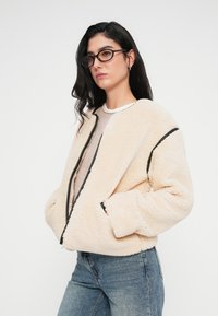 Μπουφάν bomber από κρεμ φλις με φερμουάρ και μαύρες λεπτομέρειες. Διαθέτει δύο πλαϊνές τσέπες και άνετη εφαρμογή.