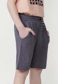 Sivé šortky vyrobené z jemného materiálu s elastickým pásom, bočnými vreckami a čierno-bielym šnurovaním.