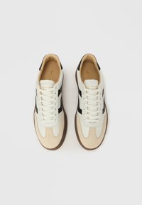 Weiße und beigen Sneaker mit schwarzen Akzenten, aus Leder und Wildleder, runde Zehenpartie, flache Schnürsenkel und profilierte Gummisohle.