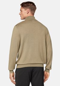 Beige knit sweater with a high, folded collar. Long sleeves and a slightly loose fit, featuring a textured pattern.
