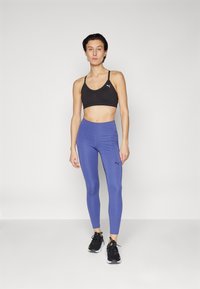 Svart sports-BH, blå leggings og svarte joggesko. Leggingsene sitter tett og har en glatt tekstur, samt en subtil logo-detalj på siden.