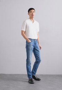 Biele polo tričko s krátkym rukávom, svetlo modré džínsy a čierne topánky. Úzky strih s minimálnou textúrou a klasickým strihom.