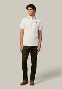 Koszulka polo w kolorze off-white z bawełny z kontrastowym kołnierzykiem, w zestawie z ciemnozielonymi spodniami i brązowymi zamszowymi butami. Posiada logo na piersi.