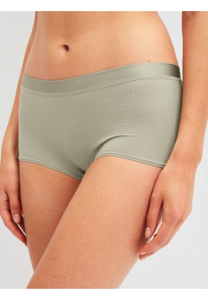 Vrouwelijke torso en bovenbenen, draag een lichtgroene naadloze boyshort-stijl onderbroek, hand ontspannen langs het lichaam, tegen een effen achtergrond.