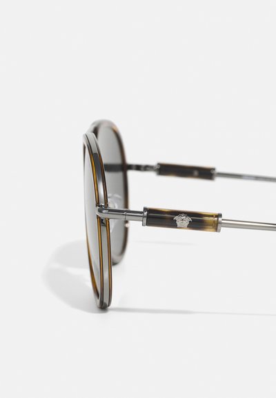 Ochelari de soare rotunzi cu un model de țestoasă, accente metalice și brațe subțiri cu detalii ale logo-ului. Lentilele închise la culoare oferă un contrast.