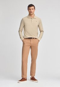 Beżowa koszulka polo z długim rękawem i kołnierzykiem, khaki dopasowane spodnie i brązowe sneakersy. Gładka faktura, minimalne logo na koszulce.