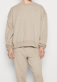 Felpa beige con texture a coste, scollo a girocollo, vestibilità oversize e spalle scese. Include pantaloni da tuta beige coordinati.
