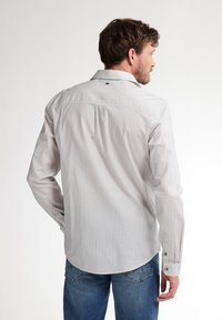 Camicia a maniche lunghe di colore grigio chiaro con sottili righe verticali. Realizzata in un tessuto testurizzato, presenta un colletto a bottone e un orlo arrotondato.