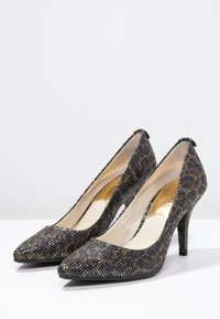 Talons hauts à motif noir et or avec un bout pointu et un talon aigu mince. Fabriqués en matériau synthétique texturé.