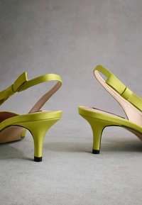 Talons slingback en satin vert citron avec un accent en nœud, talons fins et un embout de talon noir contrasté. Texture lisse avec un design de bout pointu.