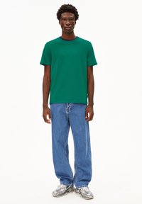 Grünes Kurzarm-T-Shirt mit Rundhalsausschnitt, kombiniert mit hellblauen, lässigen Jeans und grauen Sneakers mit strukturiertem Muster.