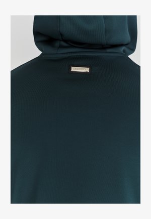 Mørk teal hoodie lavet af glat, strækbart stof. Har et logo-patch i sølv på ryggen, med en afslappet pasform og hætte design.