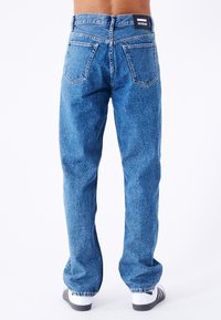 Blå denimjeans med en afslappet pasform, fem-lomme design og synlige syninger. Livremmen har et sort mærke på bagsiden.
