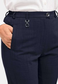 Marineblauwe broek met een gestructureerd patroon, elastische tailleband, zijzakken en een zilveren hardware-accentdetail op de taille.