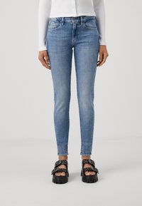 Jeans de ganga azul skinny com um efeito desbotado, cinco bolsos e um design justo. Combinados com sandálias de plataforma chunky pretas.