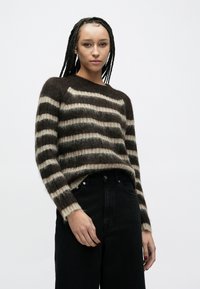 Pulover cu dungi, din tricot moale și pufoasă, cu dungi maro închis și crem, guler rotund și mâneci lungi. Asortat cu blugi negri cu talie înaltă.