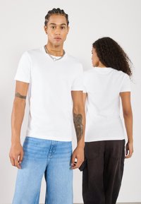 Hvide kortærmede T-shirts lavet af bomuld med rund halsudskæring. Én model står vendt mod kameraet, mens en anden står med ryggen til.