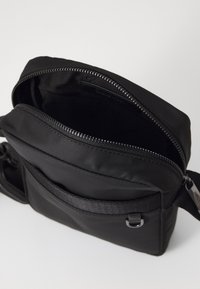 Borse a tracolla nera in tessuto con chiusura a zip, superficie testurizzata, tracolla regolabile e tasca esterna. L'interno sembra spazioso e foderato.
