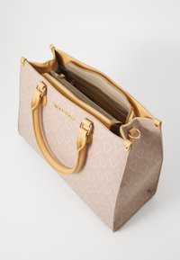 Μπεζ τσάντα με υφασμάτινο σχέδιο, με ανοιχτό καφέ χερούλια, φερμουάρ και ασημί μεταλλικά στοιχεία.