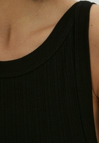 Top de tirantes negro con textura acanalada, escote redondo y detalles de costura visibles. Vista en primer plano que muestra las características del tejido y el diseño.