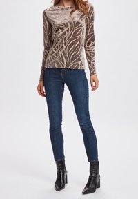 Långärmad, brun sammetstopp med ett beige lövmönster, i kombination med mörkblå skinny jeans och svarta ankelboots med klack.