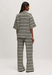 Gestreiftes Strick-Ko-Ord-Set in Creme und Schwarz, bestehend aus einem lässigen Kurzarmoberteil und weitem Hosenbein, mit einem strukturierten Muster.
