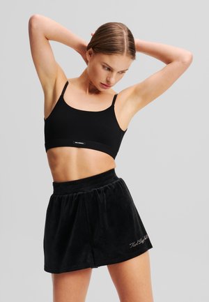 Black cotton sports bra with thin straps paired with a black velvety skirt featuring an elastic waistband and embroidered detail.