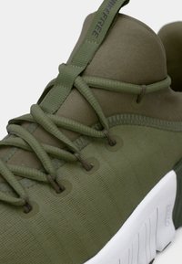 Green athletic shoe featuring a textured fabric upper, light lacing system, and a contrasting white sole with subtle ridges and branding.