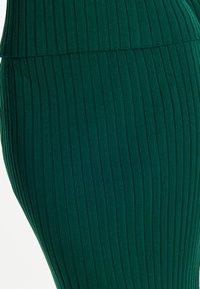 Gonna a coste verde con vita alta, texture verticale e forma aderente. Il tessuto sembra morbido ed elastico.